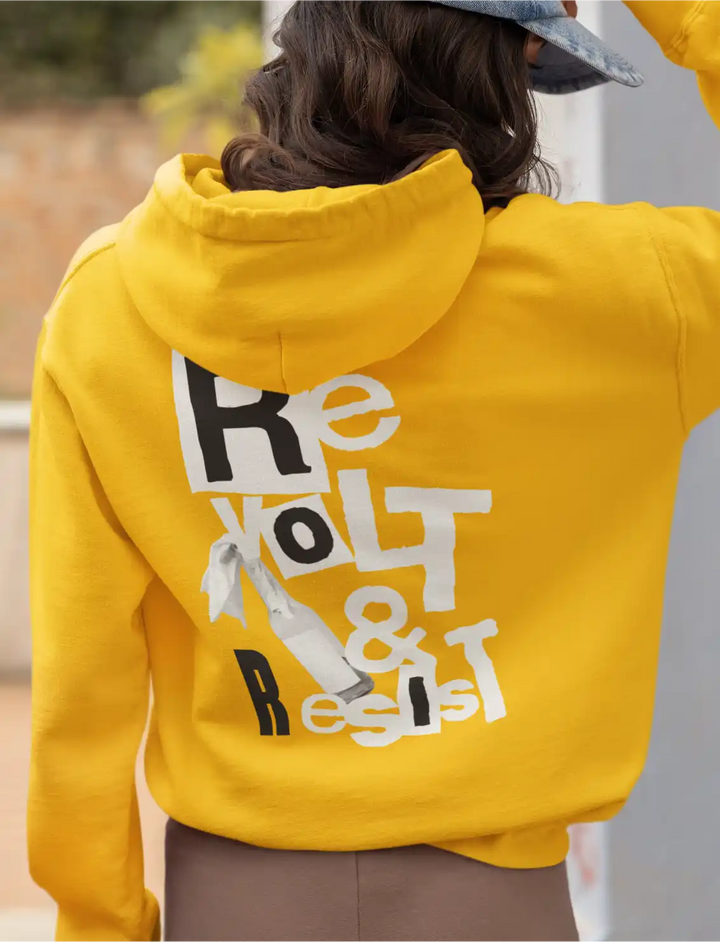 a female model wearing a golden yellow sapienwear women's hoodie with the "revolt and resist" graphic on the back side